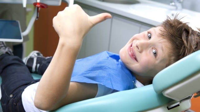 Children's dentistry patient giving thumbs up during dental checkup and teeth cleaning visit