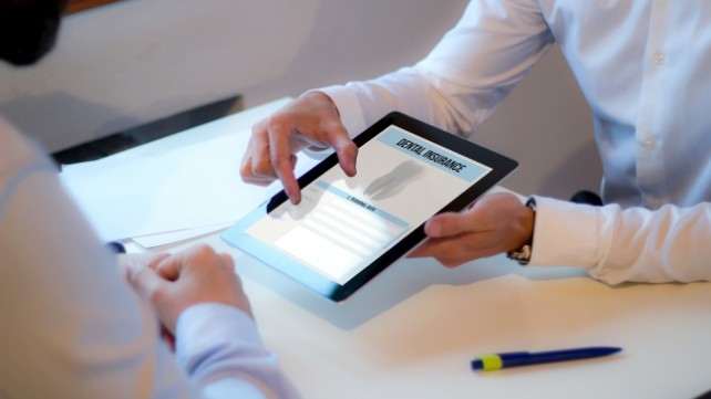 Dentist and dental patient looking at dental insurance forms on tablet computer