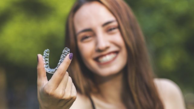 Smiling woman holding a Sure Smile clear aligner